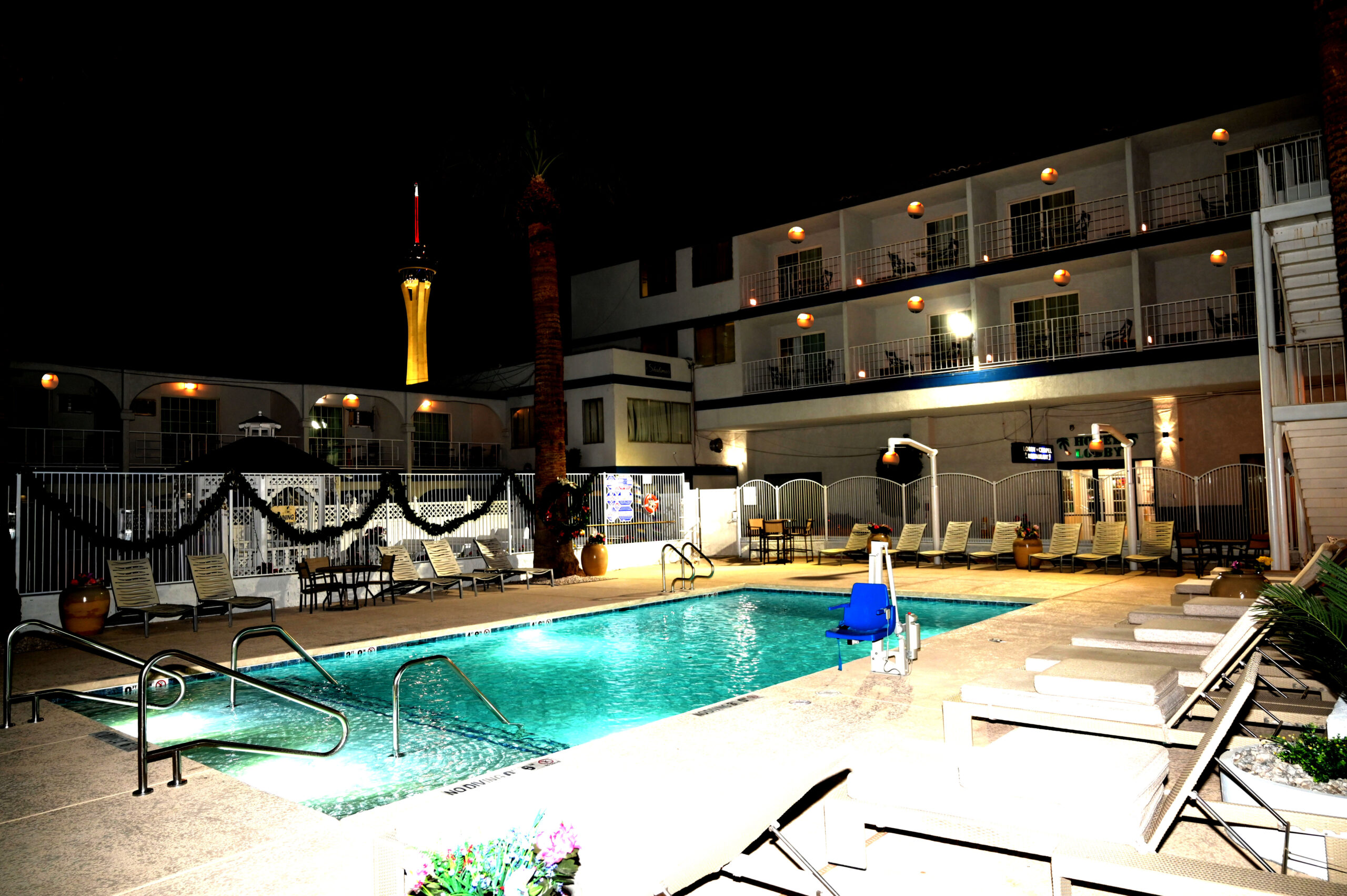 A nighttime view of a hotel pool area with lounge chairs and the hotel building in the background.